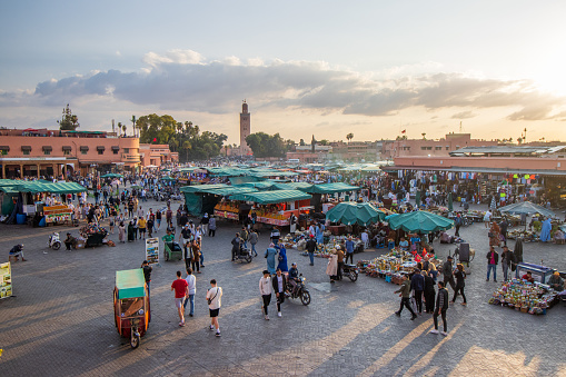 Many market stalls and people walking around Djemma el Fna Square in Marrakesh, Morocco, at dusk.