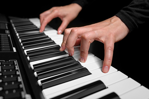 Playing a synthesizer on a dark background. The musician plays the synthesizer.