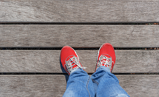 Legs in red sneakers against the background of a wooden floor.