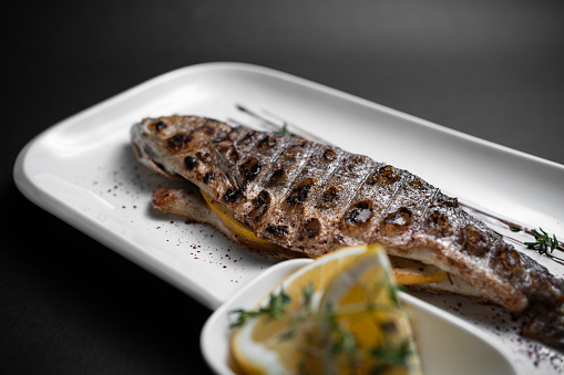 closeup of baked or fried fish with spice and lemon on plate on dark background
