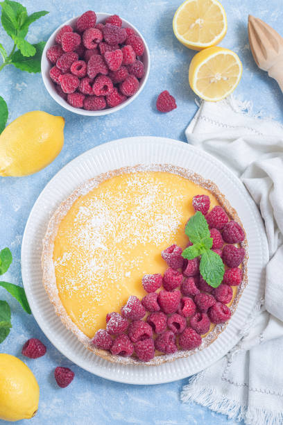 Lemon tart, garnished with fresh raspberry, icing sugar, mint, vertical top view stock photo