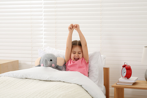 Cute little girl stretching and yawning in cosy bed
