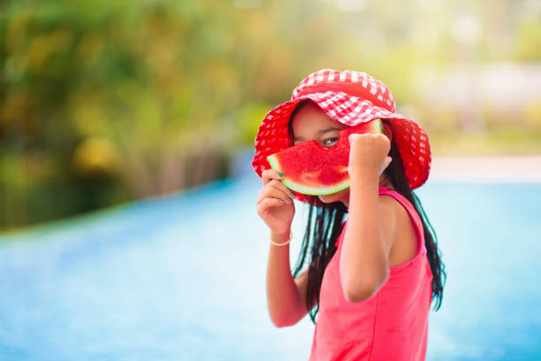 Child with watermelon in swimming pool. Summer sun and water fun. Healthy fruit snack for kids. Tropical fruits in family vacation. Travel with children. Little girl on beach holiday.