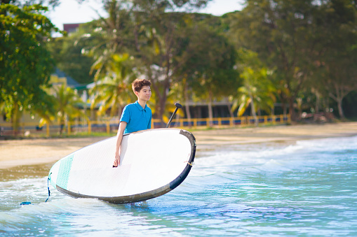 Child on stand up paddle board. Water fun and beach sport for kids. Little boy on surf board. Healthy outdoor sports for summer vacation on tropical island. Holiday activity. Surfer exercising.