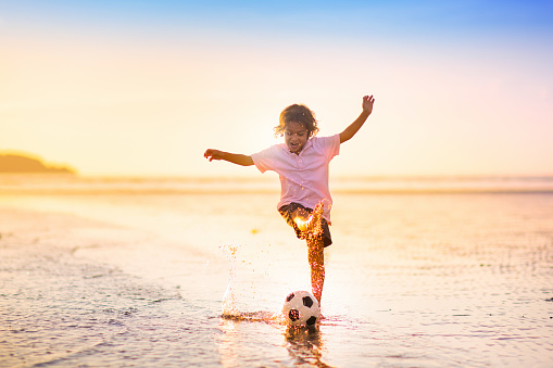 Kids play football on tropical beach at sunset. Cute little boy running with a ball. Travel with kids. Summer vacation on sea shore. Family holiday with children. Water sport fun.