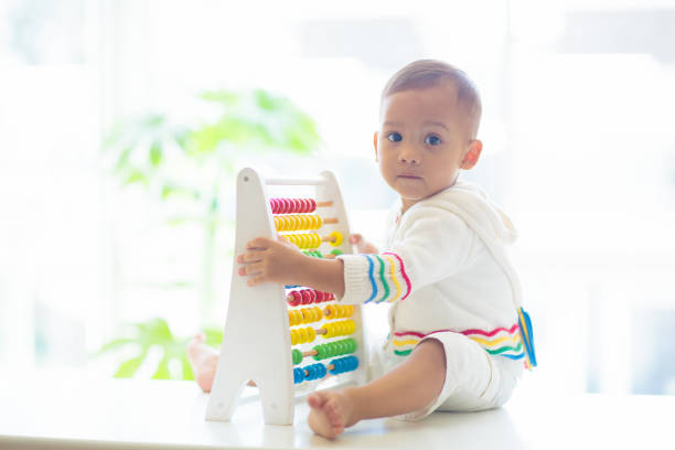 Baby boy playing with wooden abacus. Kids learn to count. Adorable smart Asian child learning numbers. Early development and education. Educational toys for infant children. Toddler kid at home.