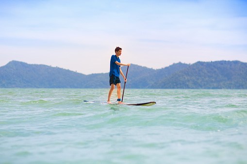 Child on stand up paddle board. Water fun and beach sport for kids. Little boy on surf board. Healthy outdoor sports for summer vacation on tropical island. Holiday activity. Surfer exercising.