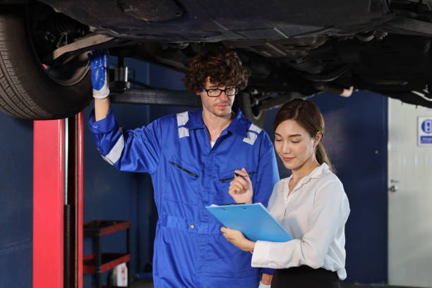 istock Man technician car mechanical in uniform showing car maintenance service report on clipboard at repair garage station. Auto mechanic give customer discussion on her vehicle repairs problems condition 1495233010