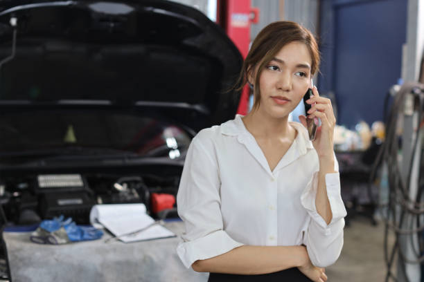 istock Young woman customer using smart mobile phone and calling insurance agent to get help or support at repair garage station with breakdown car blurred background. Concept of car center repair service. 1495233079