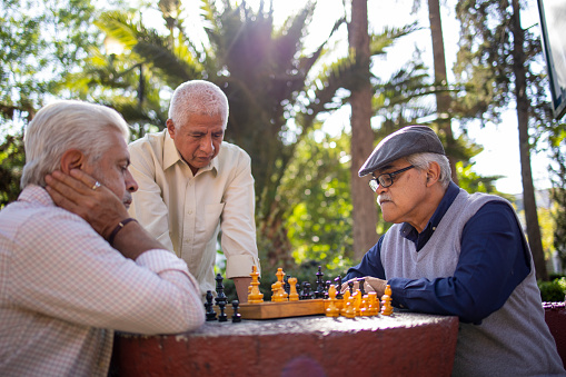 Three senior Latin friends playing chess at the park