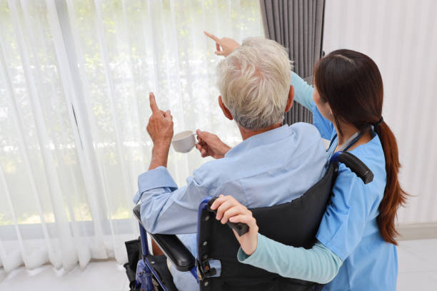 istock Rear view happy caregiver helping senior elderly man with wheelchair while pointing something at retirement house. Asian smiling nurse taking good help care and support of elder patient at house. 1495235852