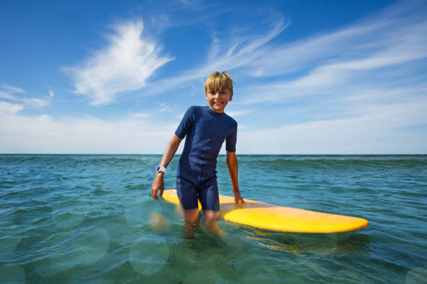 Happy young surfer boy with surfboard have fun on beach, riding on small ocean waves. Summer adventures, active families, parents and kids lifestyle, sports activities on school holiday with kids