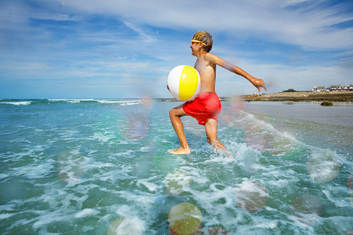 Young boy in orange sunglasses in sea with inflatable color ball view from side