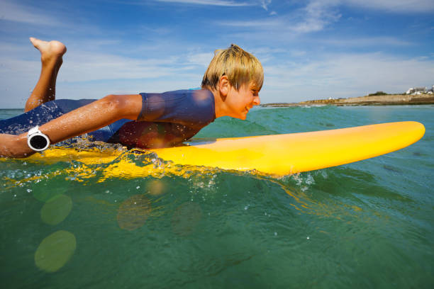 istock Cute young boy paddle on orange surfboard in ocean 1495237249