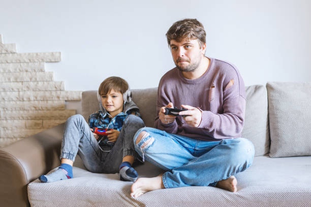 istock Father And Son Sitting On Sofa In Lounge Playing Video Game 1495237606