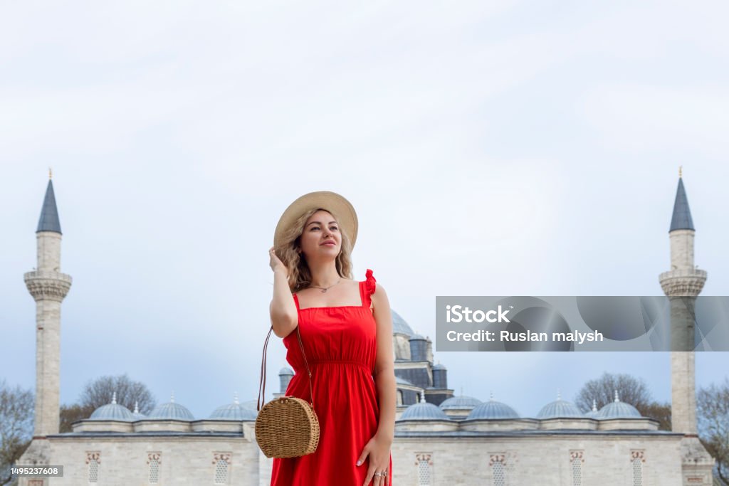A beautiful traveler girl in a long red dress and a straw hat is photographed near the ancient sights of Istanbul in Turkey. Suleiman Blue Mosque in summer. 30-34 Years Stock Photo