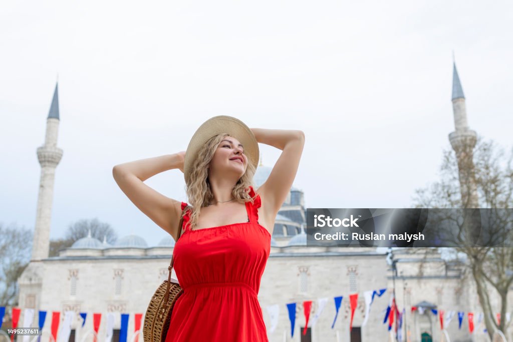 A beautiful traveler girl in a long red dress and a straw hat is photographed near the ancient sights of Istanbul in Turkey. Suleiman Blue Mosque in summer. 30-34 Years Stock Photo
