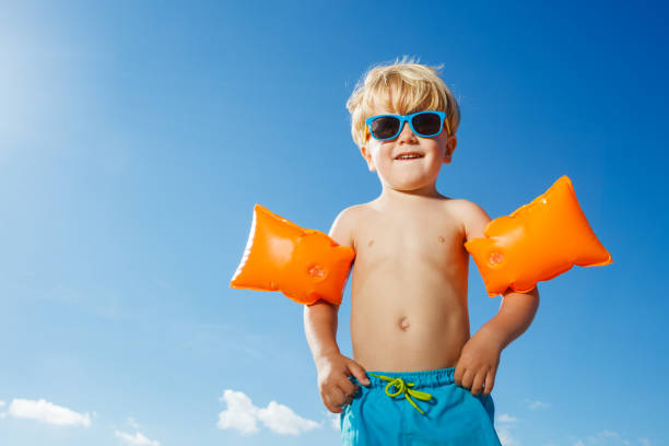 istock Boy in inflatable shoulder straps stand on the over sky at beach 1495246554