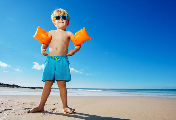 Boy in inflatable shoulder straps stand on the ocean beach stock photo
