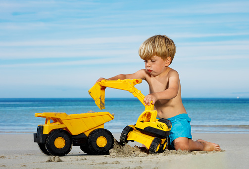 Little Caucasian boy play with trucks and excavator on the sand sea beach