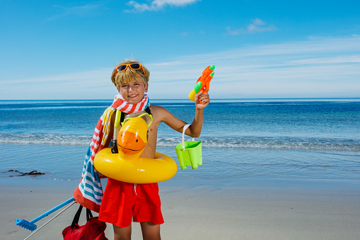 Vacation time - portrait of a boy pose with many toys inflatable duck, butterfly net scuba stand on the sea sand beach