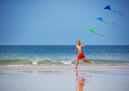Boy run fast with a kite group on the string on the beach smiling over the sky during vacation view from profile