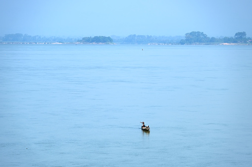 Man fishing on a wooden canoe on the Mekong river in Champasak province, Southern Laos.