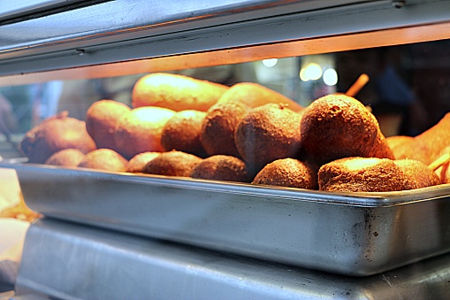 Gloriously golden freshly deep-fried crispy slightly sweet carnival fair corndogs beneath warming lights behind glass. Frankfurter dipped in cornmeal batter,fried and served on a stick. Iconic carnival fair summer food.