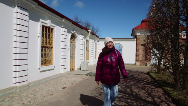 Tourist woman walking in yard and looking at white baroque style building.