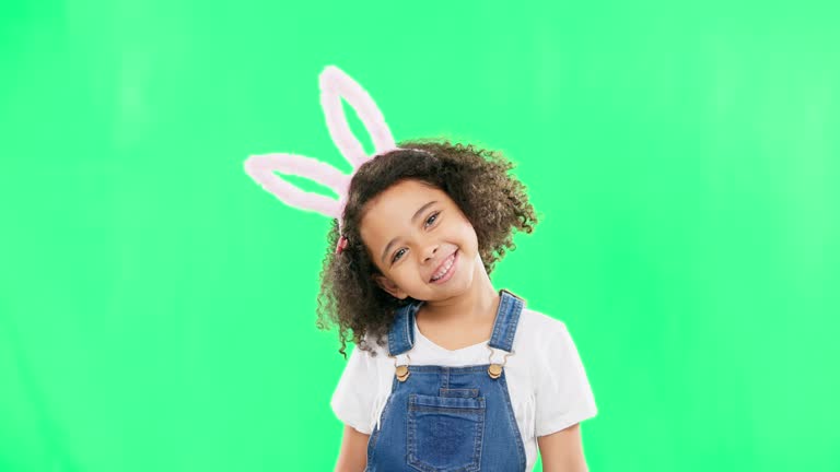 Cute, happy and face of a child with bunny ears isolated on a green screen studio background. Easter, smile and portrait of an adorable little girl smiling, looking cheerful and playful with mockup