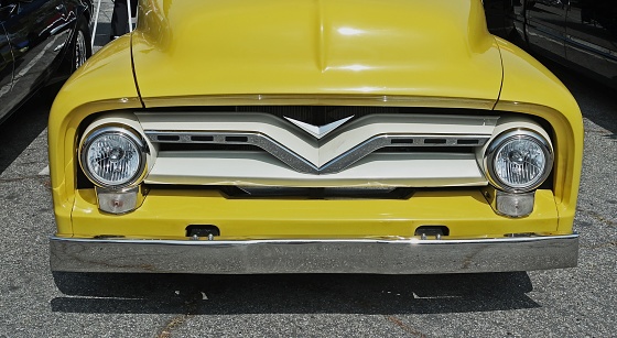 Yellow vintage truck view of front grill.   Round headlights and chrome grill.