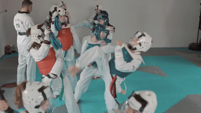 A group of boys and girls in uniforms and headwear practice taekwondo together