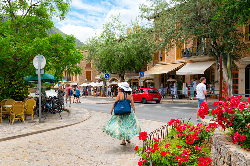 A woman walks through the picturesque streets of shops and cafes at the entrance to the picturesque village of Valldemossa, Spain.