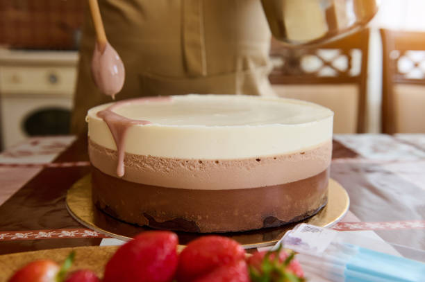 Close-up hands of pastry chef, confectioner pouring ruby pink chocolate glaze on top of a triple chocolate mousse cake stock photo
