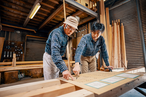 Two carpenters looking at traditional Japanese blueprints that are painted by hand onto wood.