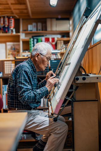 Senior male architect working at a drafting table drawing blueprints by hand