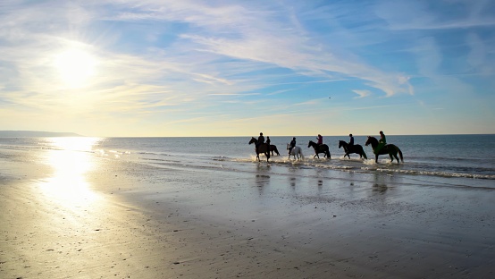 group of young riders on horseback heading towards the beach. Sea