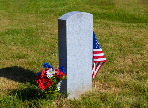 A grave stone with a USA flag with patriotic colored flowers
