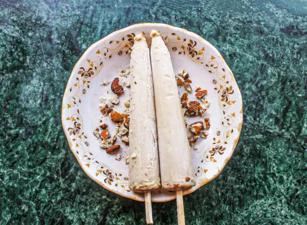 Shahi kulfi or kulfi include khoya, milk, badam, almond with stick served in dish isolated on background top view of pakistani and indian ice cream