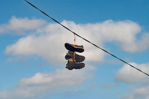 Three old runners are hanging from their laces on a power line against a blue sky