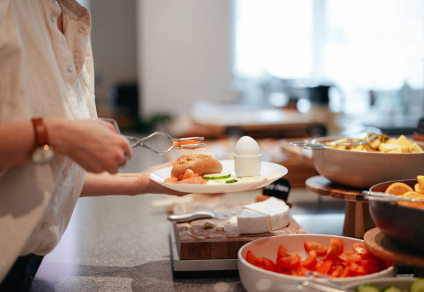 Anonymous Woman Putting Food on the Plate in the Hotel Unrecognizable woman holding a plate and choosing breakfast food from the buffet table in the hotel. buffet hotel people women stock pictures, royalty-free photos & images