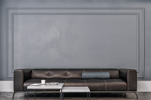 Cozy retro-chic interior with a black leather cushion sofa, two low white marble coffee tables, and decoration in front of a medium gray paneled wall background with moldings and copy space. A waiting room like a doctor's or lawyer's office. A slight vintage effect was added. 3D rendered image.
