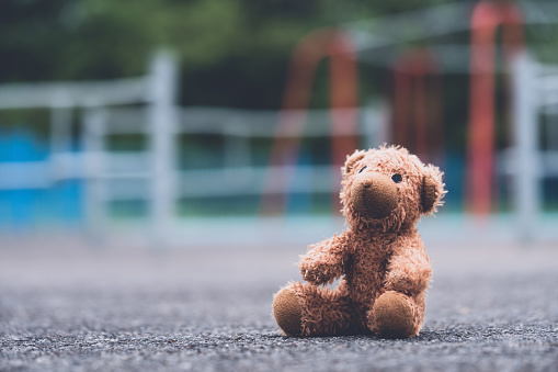 Lost teddy bear toy sitting  on playground floor in gloomy day,Lonely and sad brown bear doll sitting alone in the park, Lost toy or Loneliness concept,International missing Children day