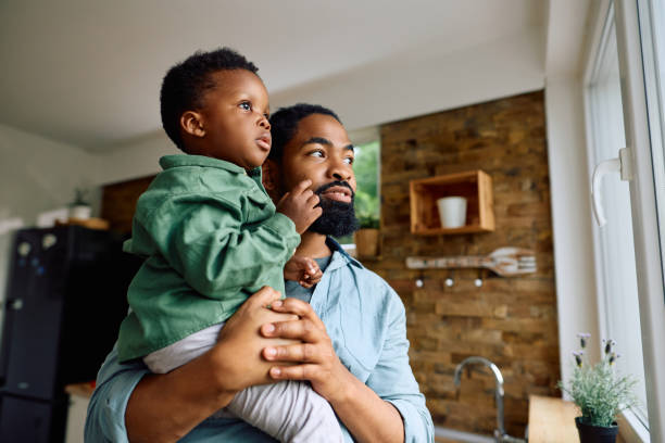 Black father and son looking through the window at home.