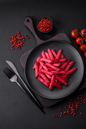 Delicious penne pasta with beets, cheese, salt and spices on a dark concrete background