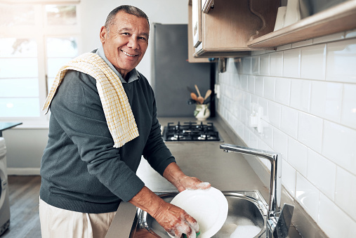 Cleaning, washing dishes or portrait of happy old man with soap water in kitchen sink in healthy home. Dirty, smile or senior male with liquid foam to disinfect, protect or prevent bacteria or germs