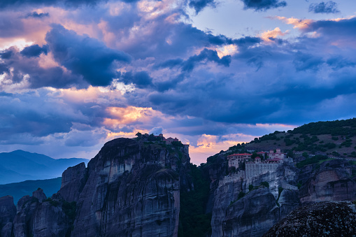 Twilight over clifftop Varlaam and Great Meteoron monasteries in Meteora, Greece. Underexposed, impressive sunset sky with clouds and sun rays. UNESCO World Heritage.