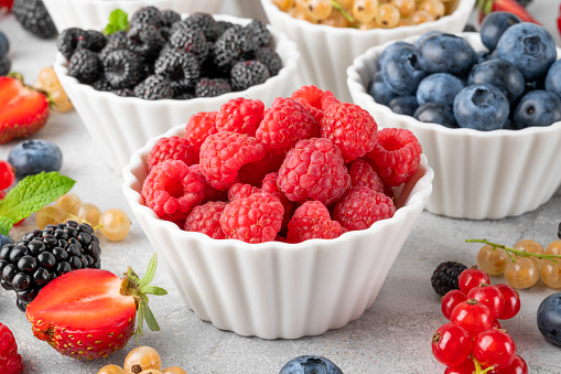 Various fresh berries in bowls on a gray concrete background. Healthy food concept