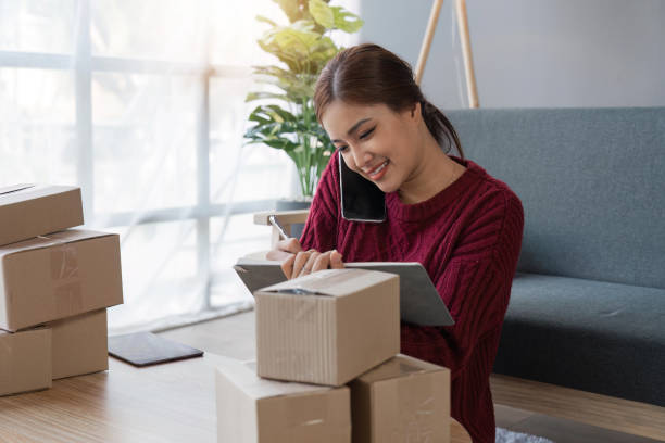 istock Cheerful small online business owner processing Internet store order for shipping, typing on laptop, speaking mobile phone, using gadgets for communication with clients 1495306131
