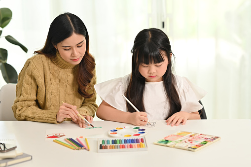 Little asian girl drawing with her mother in living room. Family home leisure concept.